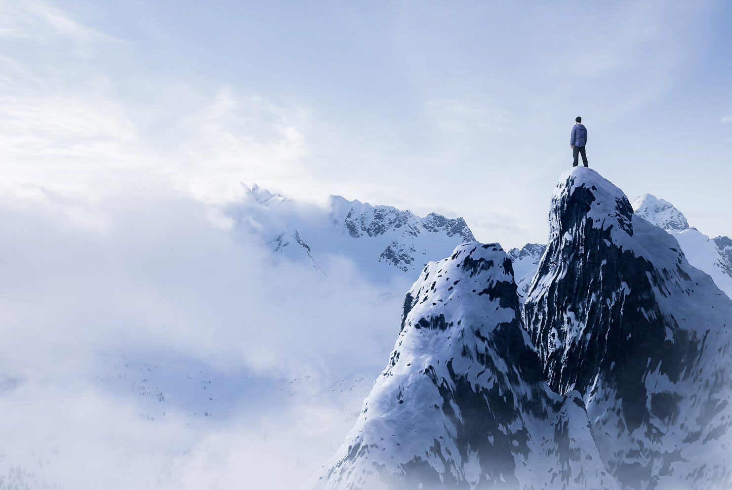 Man-Hiker-standing-on-top-of-icy-peak-with-rocky-mountains-in-background
